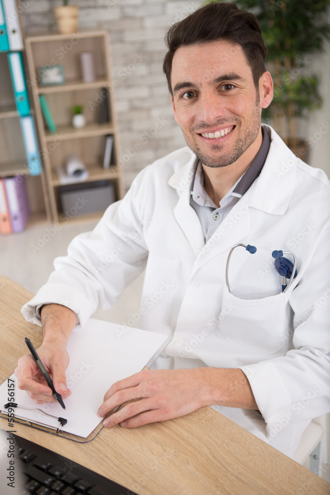 doctor looking at the camera while writing on his clipboard doctor looking at the camera while writing on his clipboard