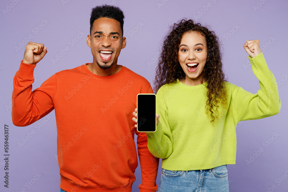 Young couple two friends family man woman of African American ethnicity wear casual clothes together use mobile cell phone blank screen look to each other isolated on pastel plain purple background.