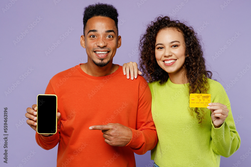 Young couple friends family man woman of African American ethnicity wear casual clothes together use blank screen mobile cell phone credit bank card order delivery isolated on plain purple background. Young couple friends family man woman of African American ethnicity wear casual clothes together use blank screen mobile cell phone credit bank card order delivery isolated on plain purple background.