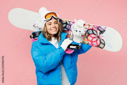 Snowboarder fun happy woman wear blue suit goggles mask hat ski padded jacket hold snowboard look aside isolated on plain pastel pink background. Winter extreme sport hobby weekend trip relax concept.