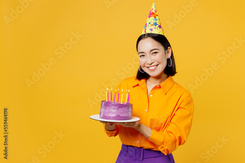 Photography Happy fun smiling young woman wearing casual clothes cap hat celebrating holding in hand purple cake with candles look camera isolated on plain yellow background