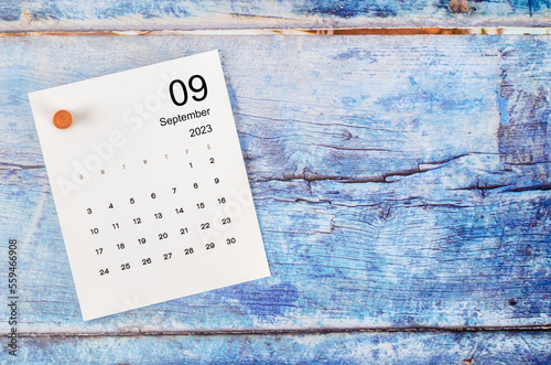 The September 2023 monthly calendar and wooden push pin on blue wooden background.