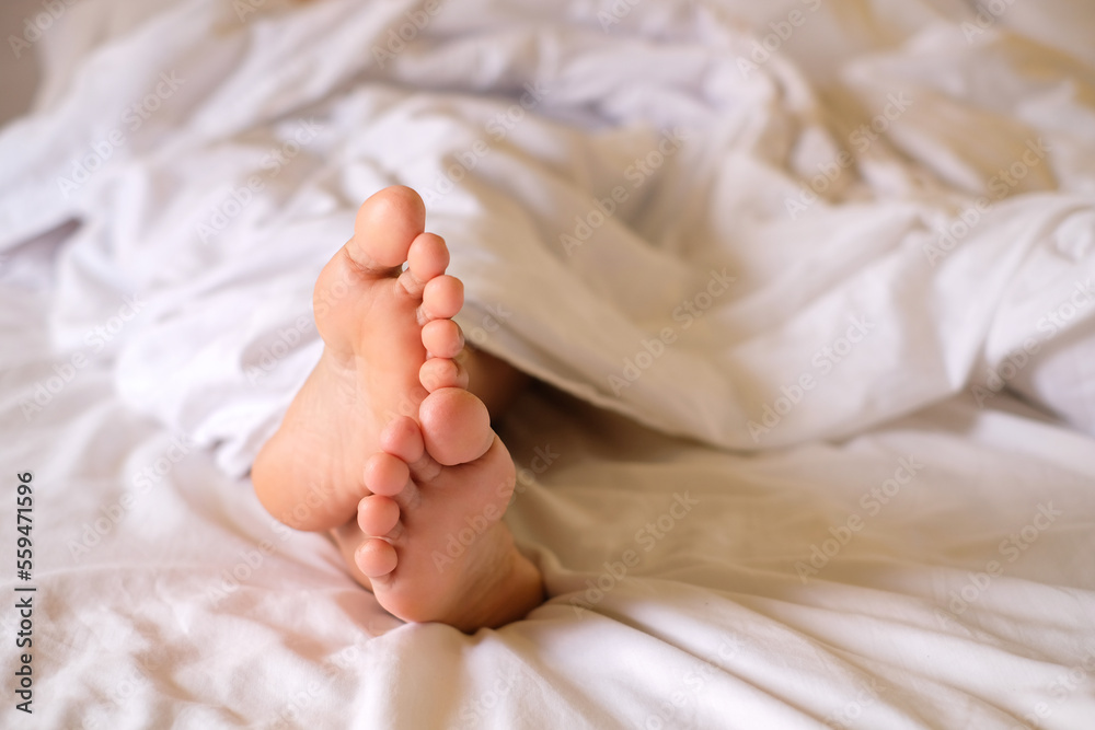 Two feet of woman awake on mattress and white blanket, morning photo, health care concept Two feet of woman awake on mattress and white blanket, morning photo, health care concept