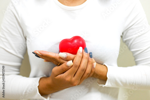 Close up on asian young woman hold red heart in the middle of breast, breast health lifestyle, self care, self love, awareness concept, health medical, insurance Concept