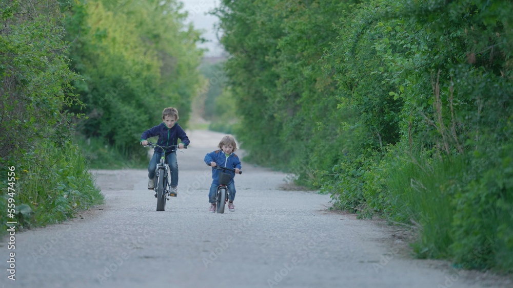 Brother riding bicycles on empty village road, children unequal competition Brother riding bicycles on empty village road, children unequal competition