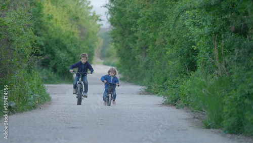 Brother riding bicycles on empty village road, children unequal competition