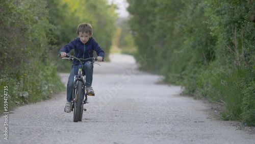 Child riding a bicycle on forest path with green trees, free childhood © MEDIAIMAG