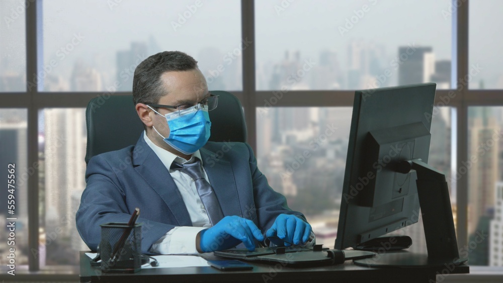 Man with suit, tie, eyeglasses, corona virus mask and gloves taping at computer Man with suit, tie, eyeglasses, corona virus mask and gloves taping at computer