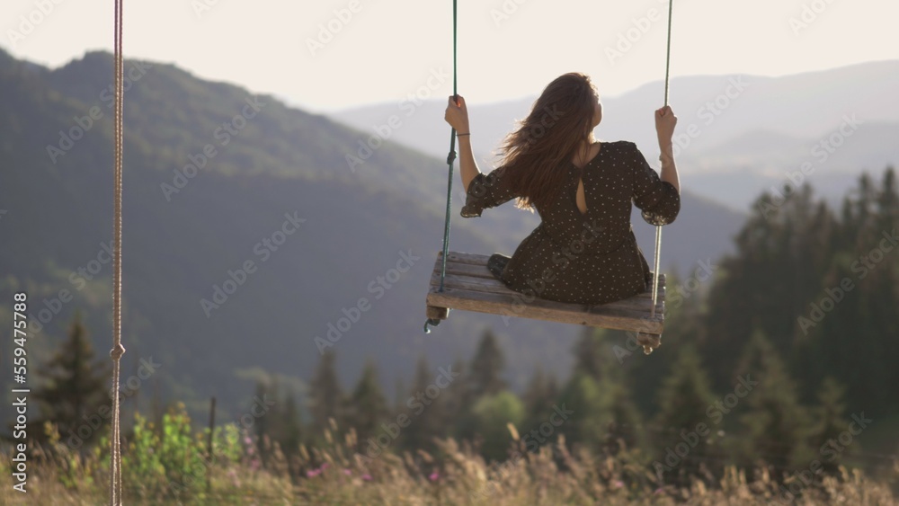 Lonely young woman enjoy freedom in a swing in front of mountain panorama
