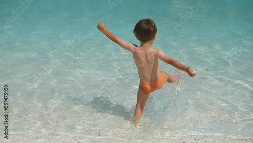 Εκτύπωση καμβά Rear view of small kid playing on beach into the shallow water of the sea