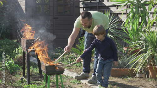 Father and son put wood pieces on barbecue grill fire
