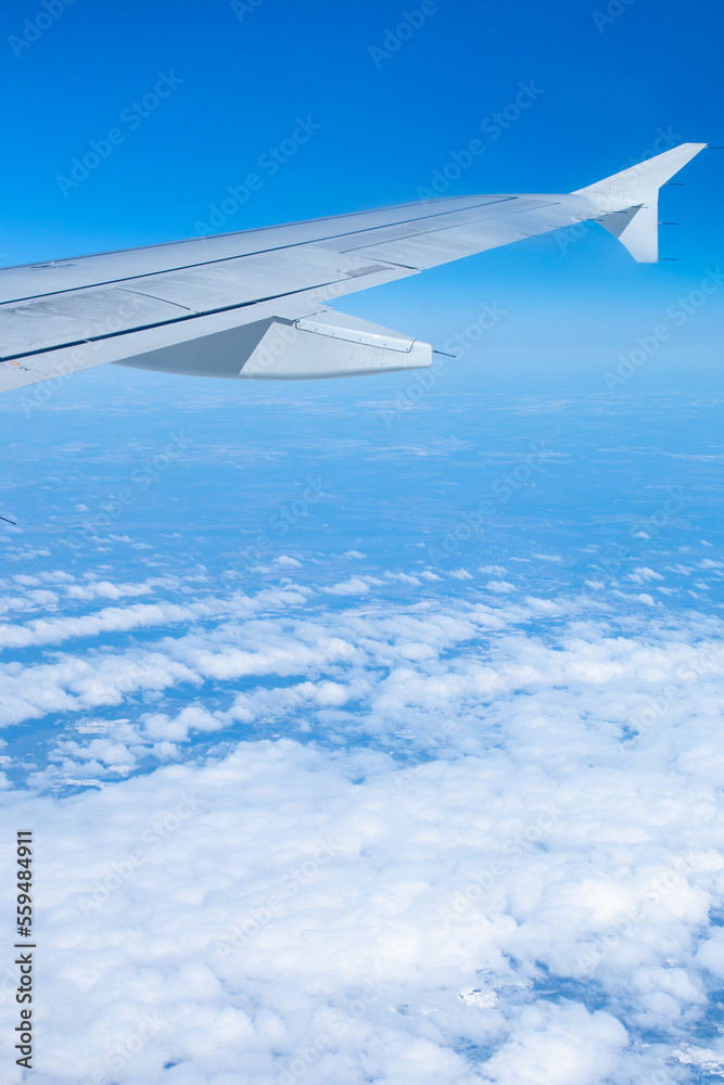 Fototapeta premium Wing of an airplane flying over white clouds and blue sky