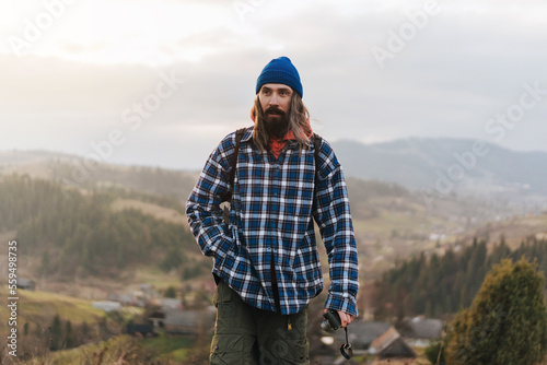 Hiker male climber with a backpack behind his back walking against the backdrop of a beautiful mountain landscape and looks into the distance.