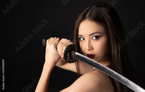 Beautiful asian woman portrait with katana samurai sword on a dark background with copy space.