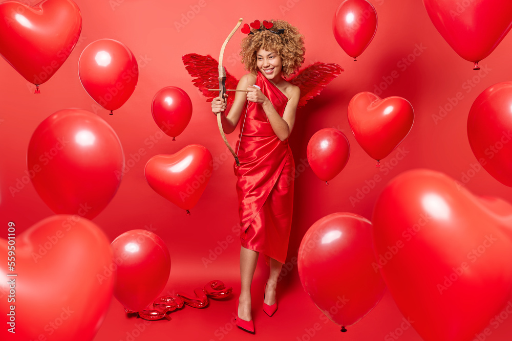 Positive woman with curly hair being in role of cupid shoots arrow ...