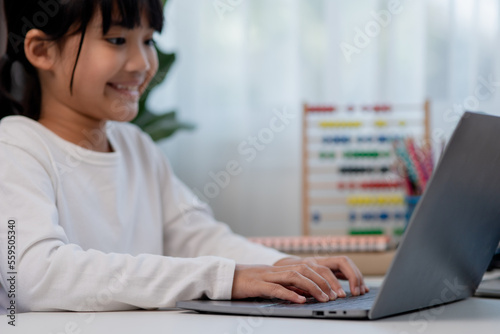 Asian schoolgirl doing her homework with laptop at home. Children use gadgets to study. Education and distance learning for kids. Homeschooling during quarantine. Stay at home © FAMILY STOCK