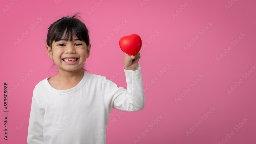 Little Asian girl holding red heart shaped application and looking at camera happily on pink. Little Asian girl holding red heart shaped application and looking at camera happily on pink.