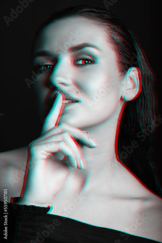 Beautiful woman with wet hairstyle portrait. Model looking at camera and making silent gesture by touching lips with finger. Red and blue color split effect applied. Futuristic looking style photo