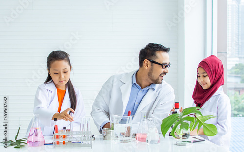 Handsome teacher  little diverse girls wearing white gown uniform  teaching  studying Science in class room at school  smiling  doing plant research experiment together. Education Concept.