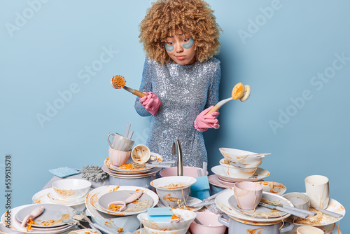 Obraz na plátně Confused shocked young woman with curly hair feels hesitant holds sponge and bru