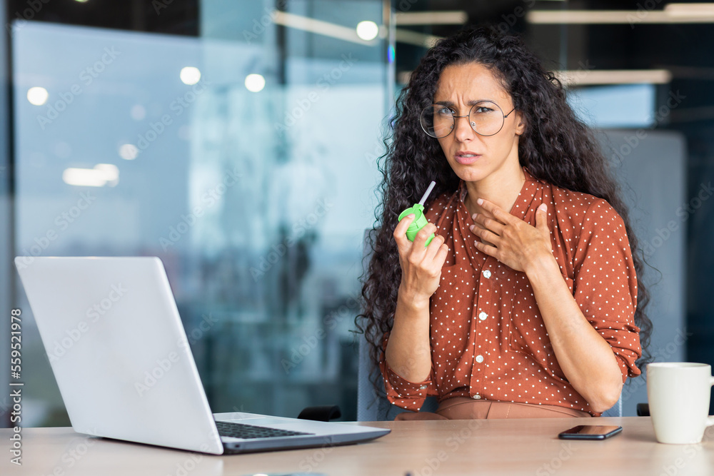 A young sick Latin American woman sits in the office at a table with a ...