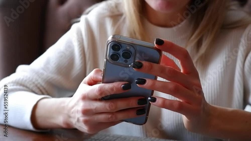 Woman hand is holding and touching iphone 13 pro and looking at the screen of mobile phone in light room.