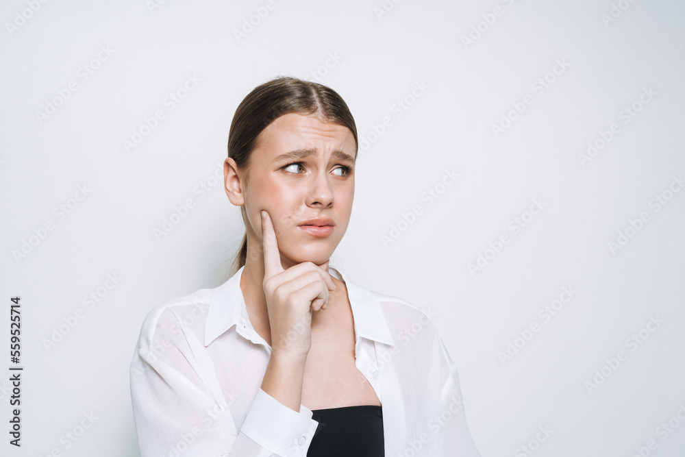 Thinking upset teenage girl student frowns in white shirt on white background Thinking upset teenage girl student frowns in white shirt on white background