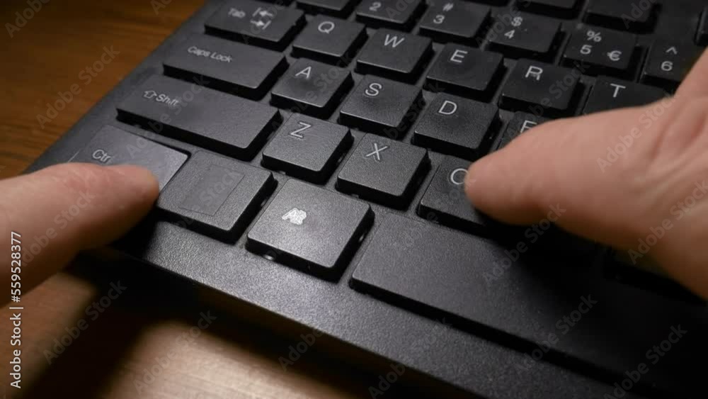 A black keyboard of a computer and a man's hands pressing the CTRL and C keys to do the copy, and then CTRL and V keys to do the paste command. Close up shot