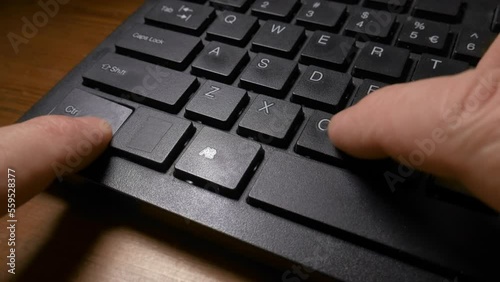 A black keyboard of a computer and a man's hands pressing the CTRL and C keys to do the copy, and then CTRL and V keys to do the paste command. Close up shot