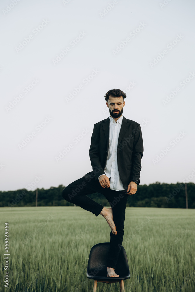 a man poses for a stylized photo shoot standing on a high chair in the middle of a green field a man poses for a stylized photo shoot standing on a high chair in the middle of a green field