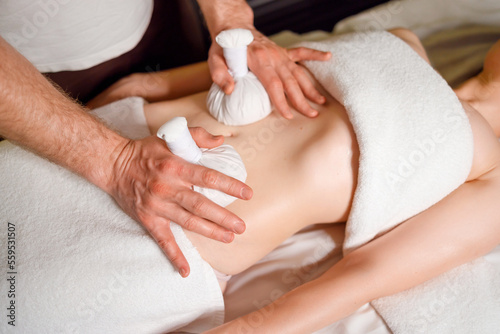 Woman having an abdomen massage with with aromatic herbal bags