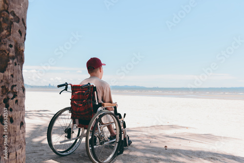 Back of young man with disability wearing a red cap on wheelchair, Activity outdoors on the beach background, Vacation on holiday and natural therapy and mental health concept.
