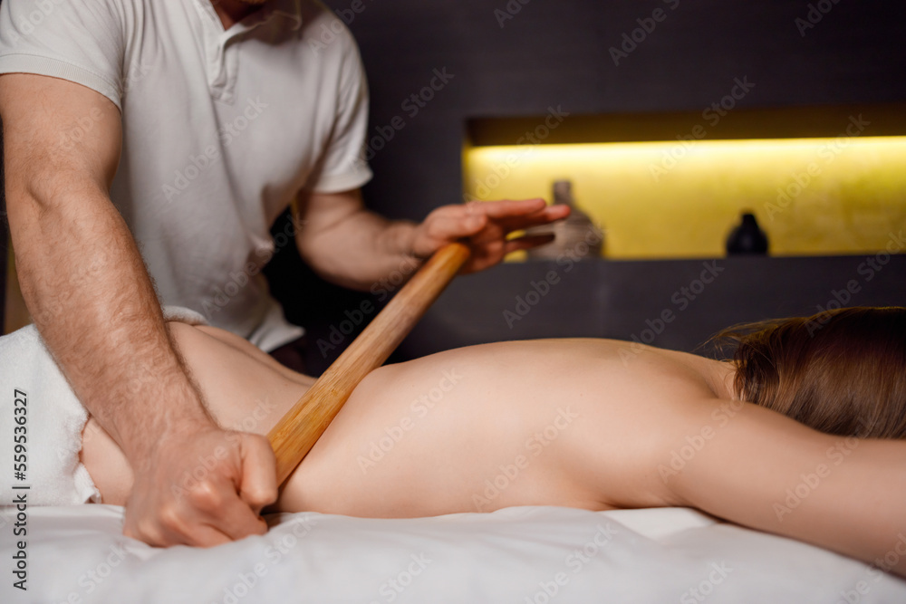 Strong male masseur doing massage with bamboo sticks to his female client