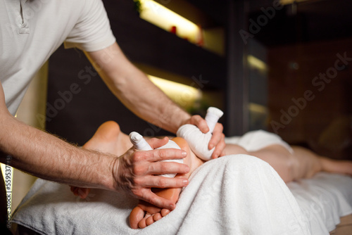 Male masseur doing a foot massage with aromatic herbal bags for his female patient in spa salon