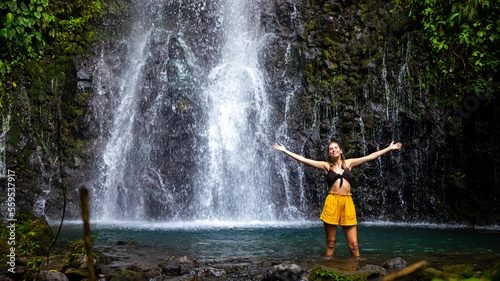 A beautiful girl spreads her arms while standing under a tropical waterfall in Costa Rica; swimming in a hidden waterfall in the rainforest; don jose waterfalls