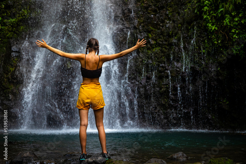 A beautiful girl spreads her arms while standing under a tropical waterfall in Costa Rica  swimming in a hidden waterfall in the rainforest  don jose waterfalls © Jakub
