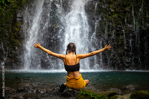 A beautiful girl spreads her arms while standing under a tropical waterfall in Costa Rica; swimming in a hidden waterfall in the rainforest; don jose waterfalls photo