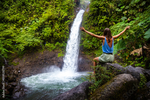 Photo A beautiful girl sits on rocks under a powerful tropical waterfall in Costa Rica