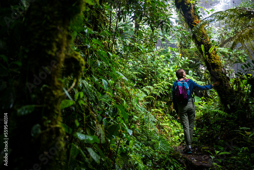 backpacker girl walks through dense jungle in monteverde cloud forest, Costa Rica; walk through fairy tale, magical tropical rainforest; wild nature of Costa Rica