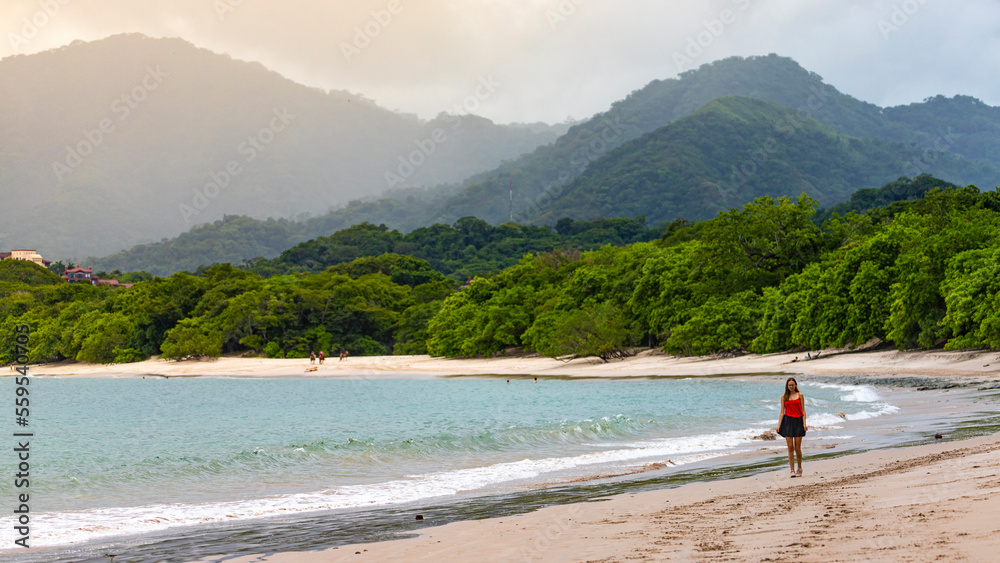a beautiful girl in a short skirt walks on the famous conchal beach on the pacific coast of Costa Rica; a paradise beach with turquoise water and green hills in the background a beautiful girl in a short skirt walks on the famous conchal beach on the pacific coast of Costa Rica; a paradise beach with turquoise water and green hills in the background