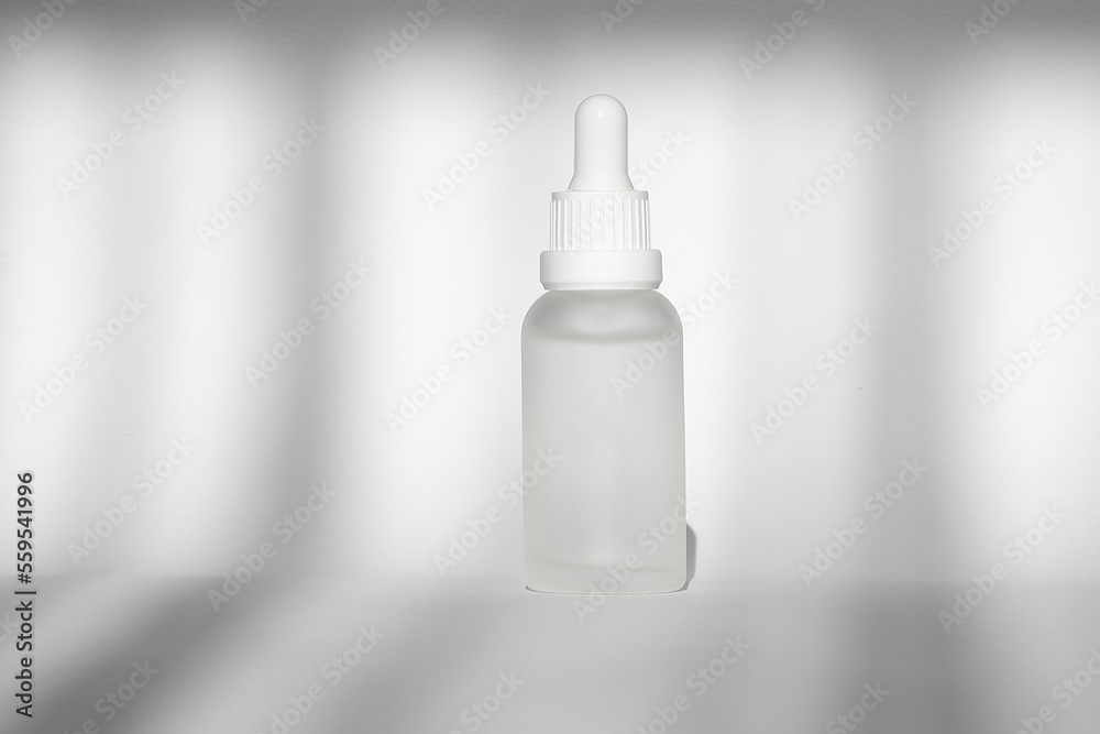 White bottles with serum, tonic or essential oil . White background with daylight with shadows. Beauty concept for face and body care White bottles with serum, tonic or essential oil . White background with daylight with shadows. Beauty concept for face and body care