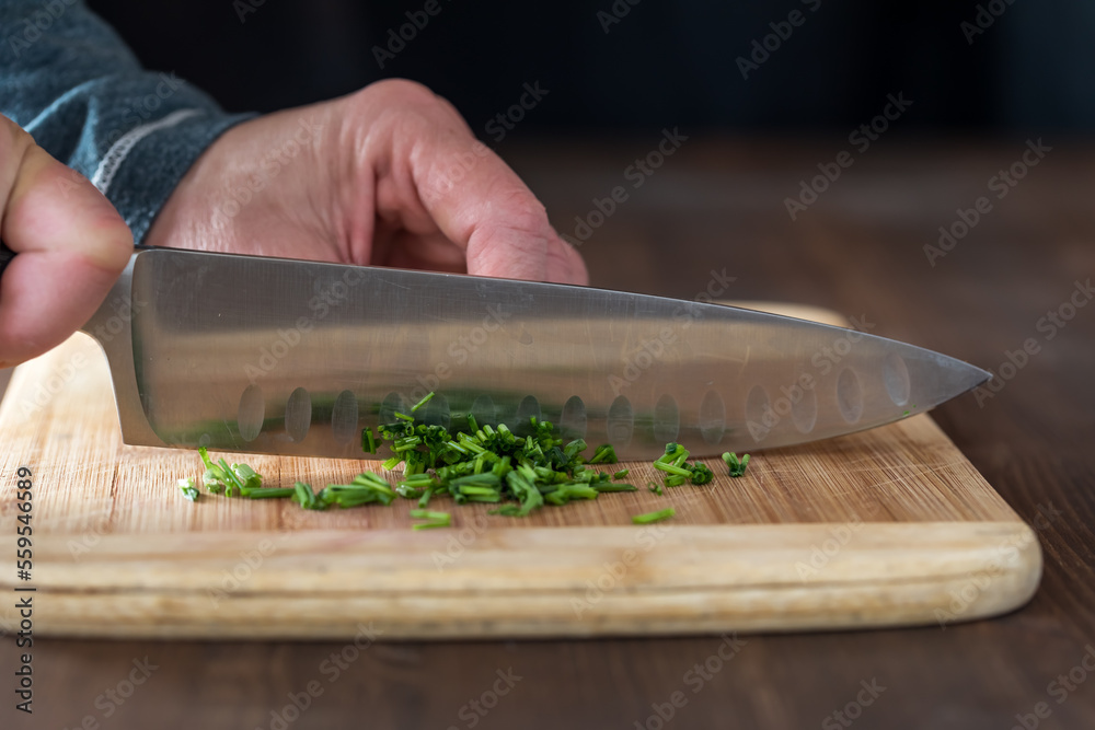 A chef's hands chopping fresh chives on a wooden cutting board. A chef's hands chopping fresh chives on a wooden cutting board.