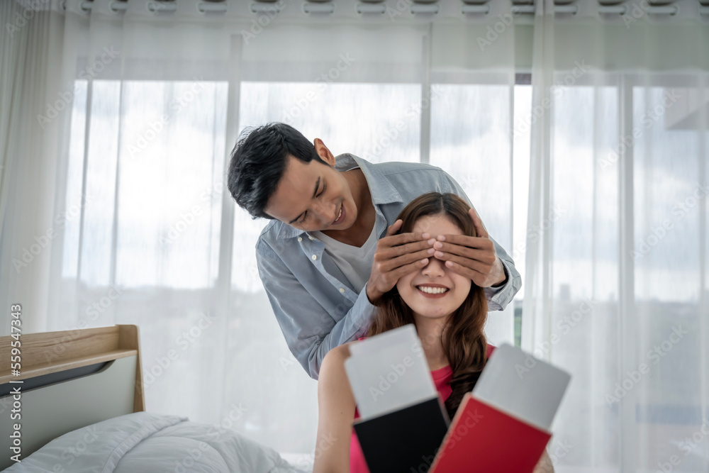 Asian couple surprises girlfriend with plane ticket and passport to hang out together on vacation in their bedroom at home Asian couple surprises girlfriend with plane ticket and passport to hang out together on vacation in their bedroom at home