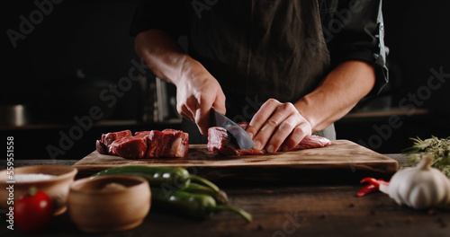 Chef sharpening his knife in front of raw piece of steak. Cooker preparing his tools for cutting meat for grilling on professional kitchen table. High quality 