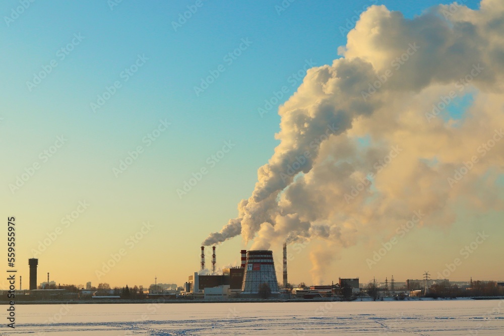 Winter clear cold morning, smoking chimneys of a power plant on the shore of a frozen lake