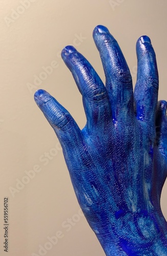 Dłoń pomalowana na niebiesko na jasnym tle. Kolorowa ręka i niebieskie palce