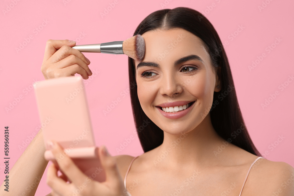 Beautiful woman with cosmetic pocket mirror applying makeup on pink background Beautiful woman with cosmetic pocket mirror applying makeup on pink background