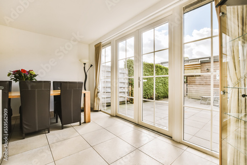 a living room with sliding glass doors and white tiles on the floor, there is a dining table in front