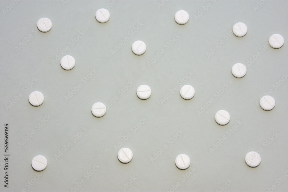 White tablets scattered on gray background form a speckled ornament. Photo for use in medicine, pharmacy, pharmaceutical production and marketing, treatment of diseases