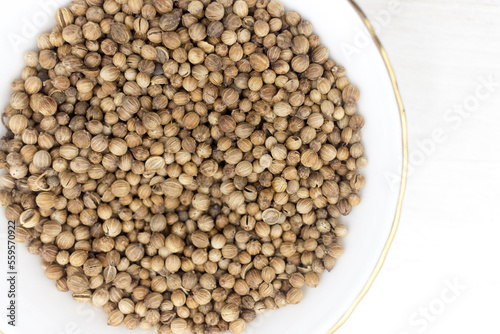Pile of Coriander seeds in a white bowl on white wooden background